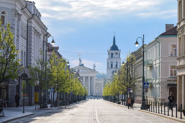 Vilnius street, in Lithuania. Street surrounded by white buildings and trees.