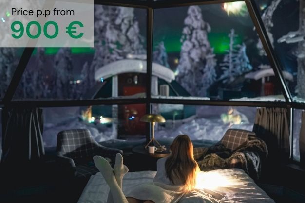 Woman on a bed looking through a glass igloo to the northern light in snow landscape