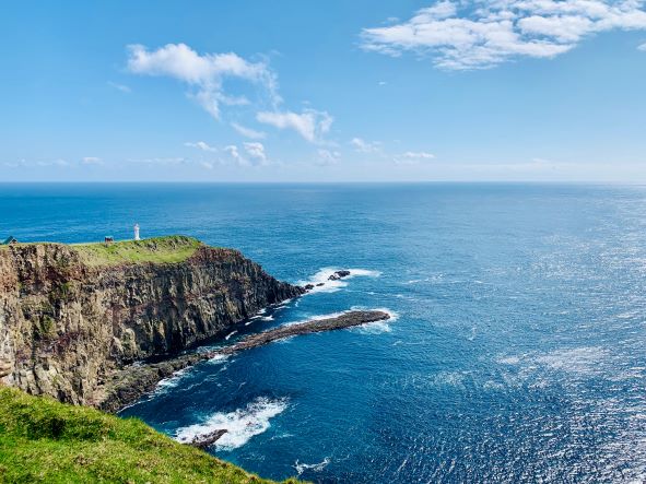 Lighthouse on the edge of a cliff with blue sky and clear water