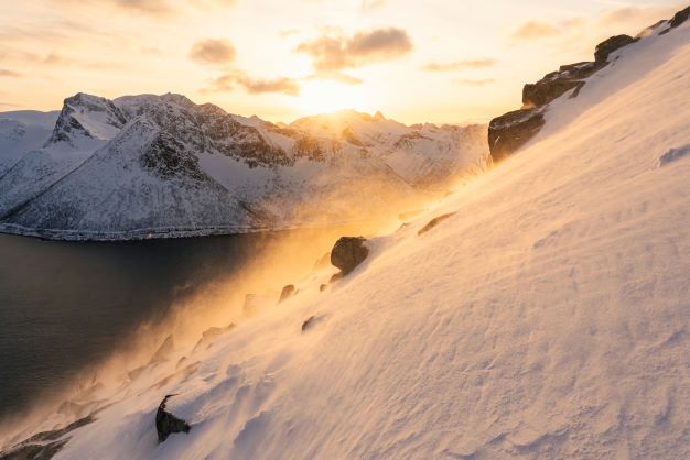 Snow covered mountains around fjords with the sunsetting behind the mountains